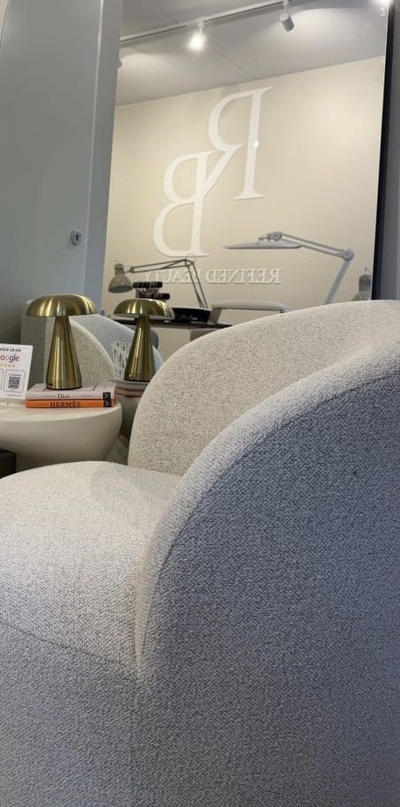 Zithoek in de salon met bouclé stoel, messing lampjes en het RB-logo op de wand